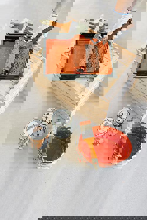 logo Närbild på målarutrustning med roller, penslar och färgburkar i orange färg, placerade på ett skyddat underlag.
