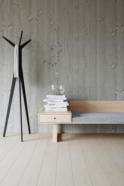 Svart klädhängare, träbänk med grå dyna och stapel böcker på golv av ljust trä.