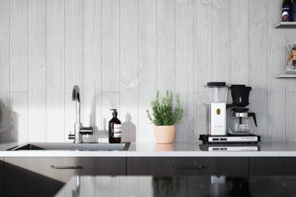 Kök med kaffemaskin, handfat, kran, tvålar och växt i kruka. Ljust träpanelvägg i bakgrunden.