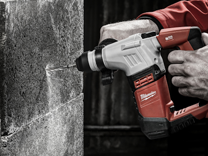 Person som borrar i en betongvägg med en röd och svart borrmaskin.