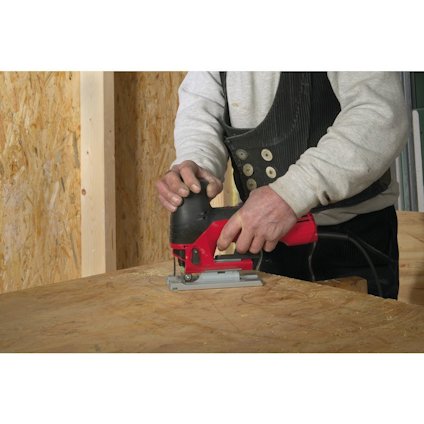 Person som använder en röd och svart sticksåg på en träyta.
