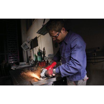Person i skyddsglasögon och blå jacka slipar metall med vinkelslip, gnistor flyger.