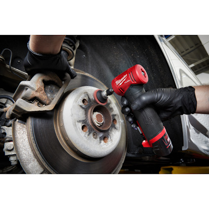 Person rengör bromsskiva med röd och svart elektriskt verktyg, klädd i svarta handskar.