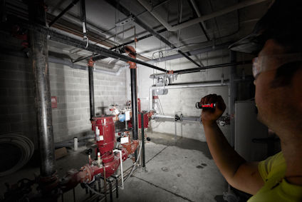 Person med ficklampa inspekterar rörsystem i en industrilokal med grå betongväggar.