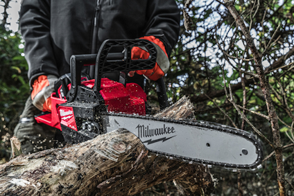 Person med röda handskar håller i en motorsåg och sågar en trädstam, omgiven av grenar. "Milwaukee" syns på motorsågen.