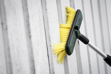 Gul borste med grön stomme på skaft rengör vit träpanel.