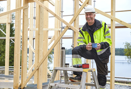 Jag vet inte vem personen är. En byggarbetare tar en paus på en stege med en kaffekopp, omgiven av en träkonstruktion.