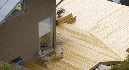 Trädäck med två stolar bredvid ett hus med stora fönster och modern design.