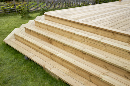 Trätrappa och däck av ljust trä i en trädgårdsmiljö med gräs runt om.