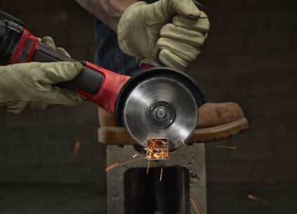 Hand med skyddshandskar använder vinkelslip för att kapa metall, gnistor flyger.
