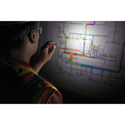 Person i bygguniform granskar en upplyst ritning med en penna.