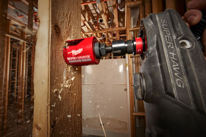 En röd hålsåg borrrar genom trä med borrmaskinen Super Hawg. Träspån sprids i luften. Bakgrund av träreglar.