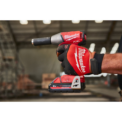 En hand i en röd handske håller en Milwaukee FUEL borrmaskin med ett batteri på 3,0 Ah.