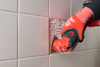 En person använder ett elektriskt verktyg med rött handtag för att skära kakelbeläggning på en vägg.