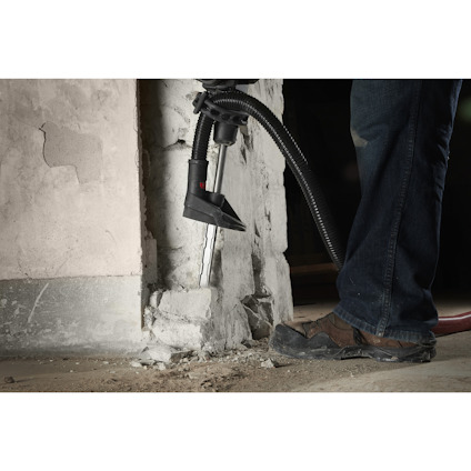 Person i jeans och stövlar som arbetar med ett munstycke anslutet till en slang mot en vägg inomhus.