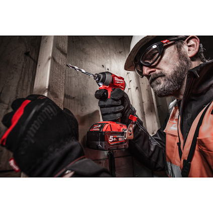 Person in safety gear using a red power drill on a wooden surface.
