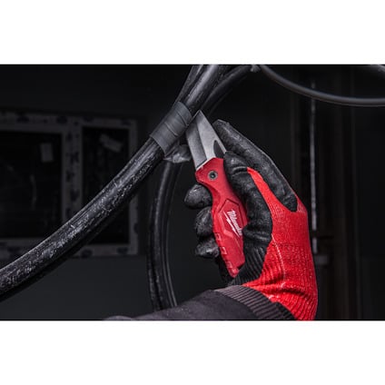 Hand med röd handske håller röd kniv och skär en svart kabel.