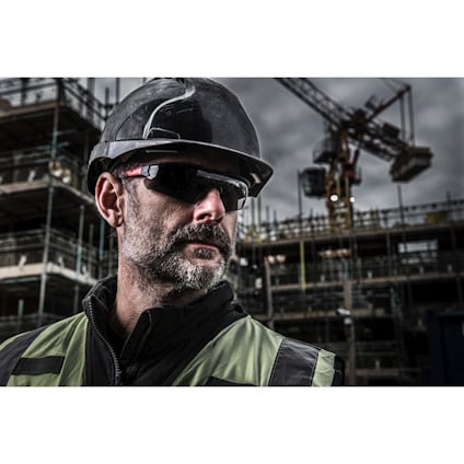 Person med svart hjälm och solglasögon står framför en byggarbetsplats med kranar och byggnadsställningar i bakgrunden.