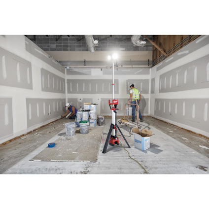 Två arbetare installerar gipsskivor i ett rum med hjälp av byggutrustning och material i olika behållare.