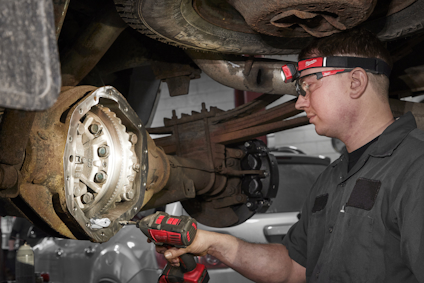 Person i arbetskläder använder ett verktyg under en upphöjd bil.