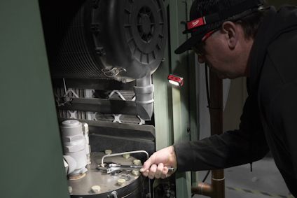Person använder verktyg på maskin med ficklampa i handen.