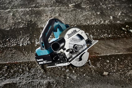 Batteridriven cirkelsåg med blått och silverfärgat hölje, placerad på ett smutsigt betonggolv.