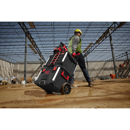 Person in work gear pulling a wheeled toolbox on a construction site. Steel framework visible.
