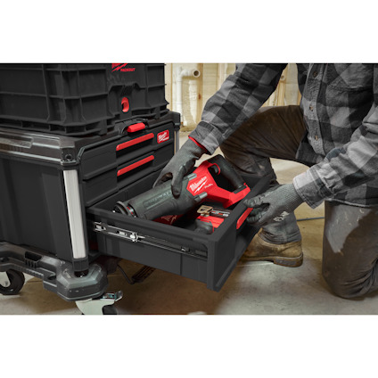 Person in workwear removes power tool from black plastic storage box with red handle and drawers in a workshop.