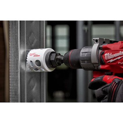 Hålsåg som borras genom metallreglar, hålls av en person i röd handske.