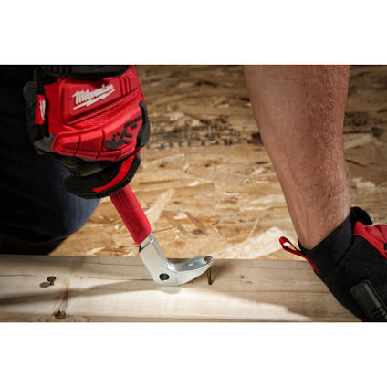 En person använder en röd hammare med klon för att dra ut en spik från trä. Personen bär handskar.