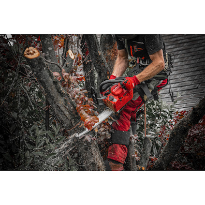 Person som sågar grenar med motorsåg, bär röda handskar och byxor.