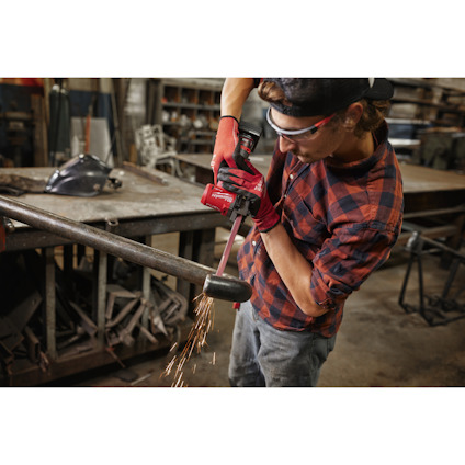 Person i skyddsglasögon och handskar slipar metallrör med vinkelslip i verkstad, gnistor flyger.