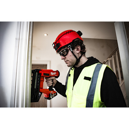 Man i hjälm och reflexväst använder en röd spikpistol inomhus.