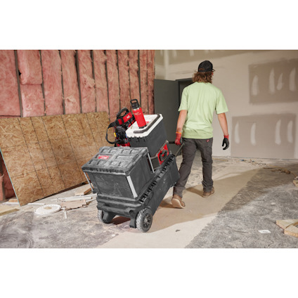 Person i ljusgrön tröja och keps drar vagna med verktygslådor i ett rum under renovering.