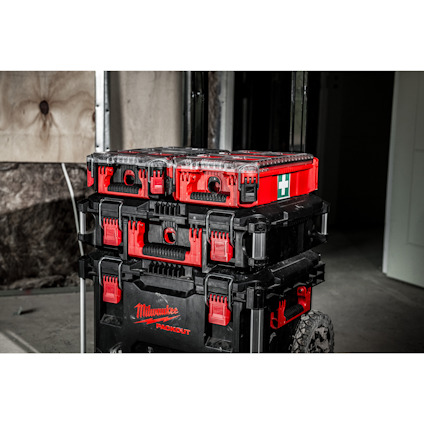 Staplade Milwaukee Packout-lådor i röd och svart färg, med ett hjulunderlag i en byggmiljö.