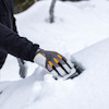 Person med handskar skrapar snö från en yta.