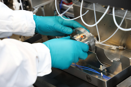 Person med blå handskar justerar metallutrustning med flera kablar i en laboratoriemiljö.