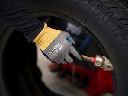 Hand med handske applicerar substans på ett bildäck med pensel.