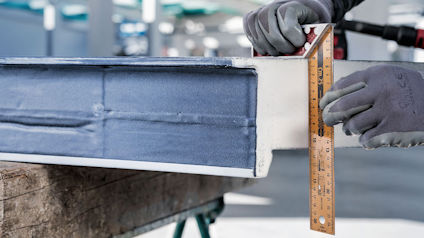 Händer mäter en metallbalk med en vinkelhake.