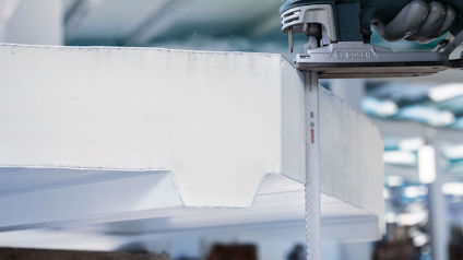 En såg skär genom vitt isoleringsmaterial i en industrimiljö.